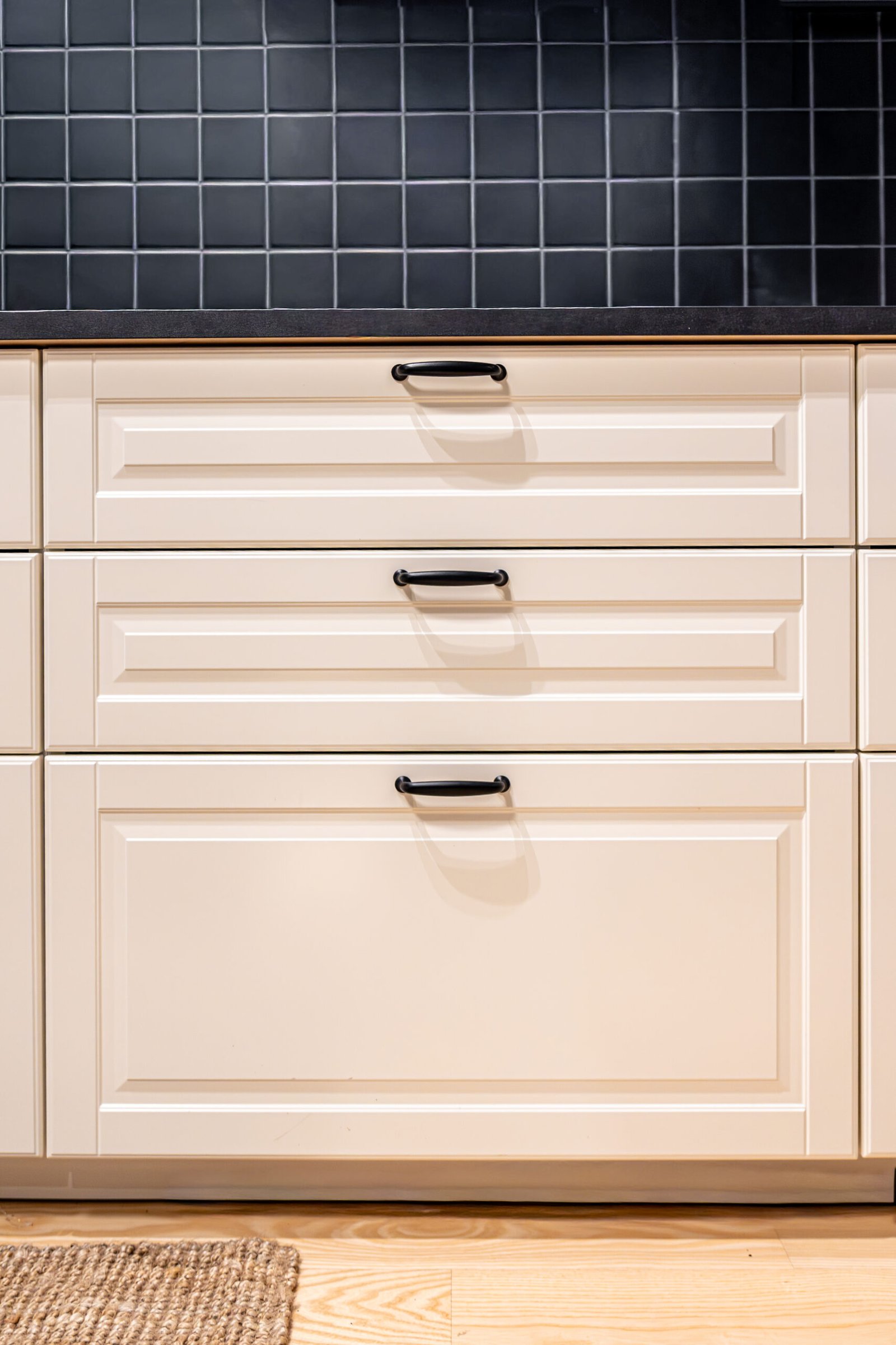 Front view of light cabinet fronts with black handles and graphic tile wall. Clean lines and organized mood for trendy home decor and interior design themes.